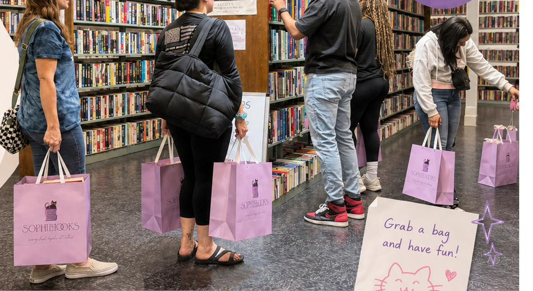 Shoppers carrying lilac Sophibooks bags along the shelves at the fill-a-bag sale